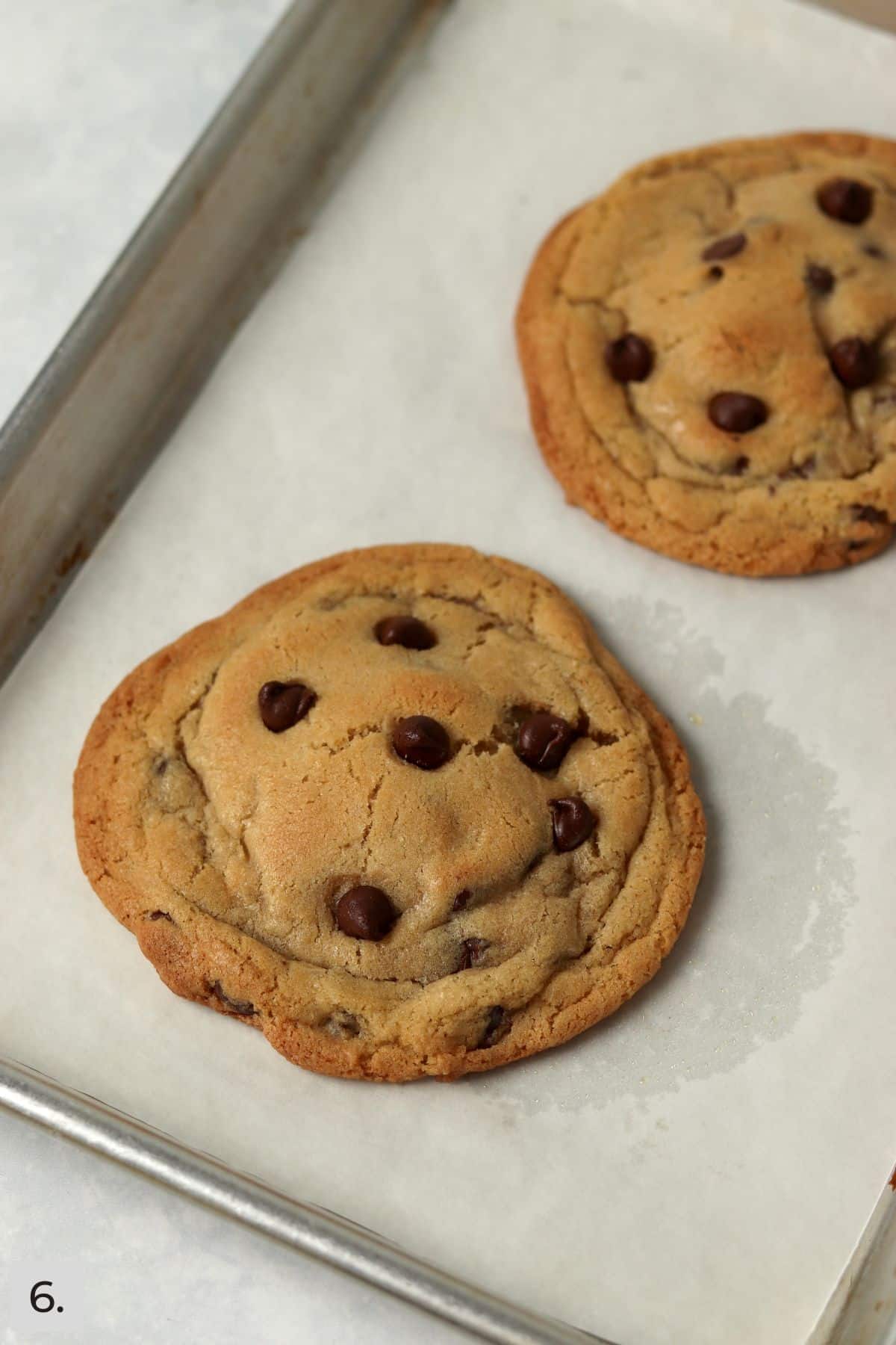 Two chocolate chip cookies on a small baking sheet.