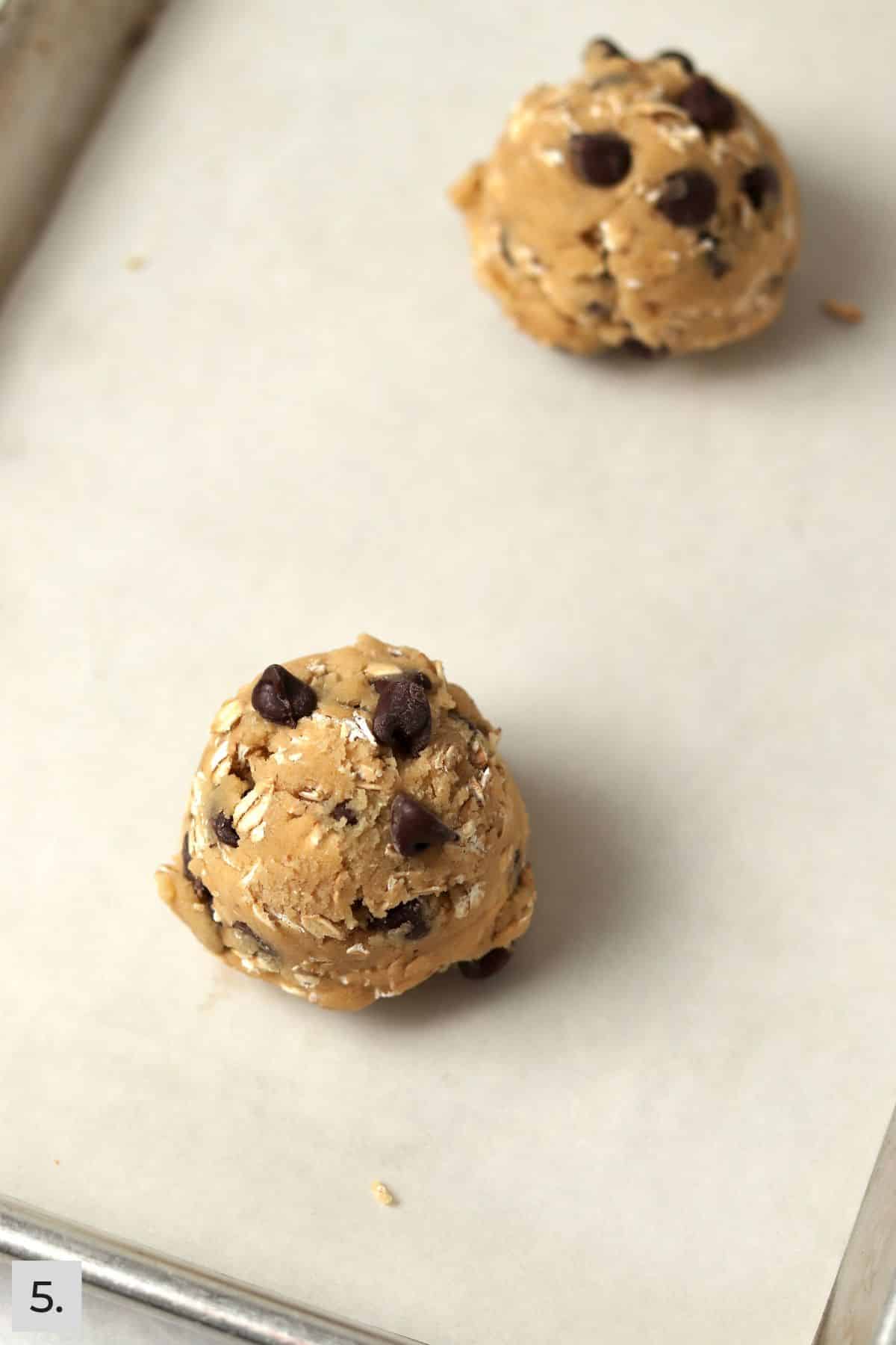 Two oatmeal chocolate chip cookie dough balls on a small sheet pan.