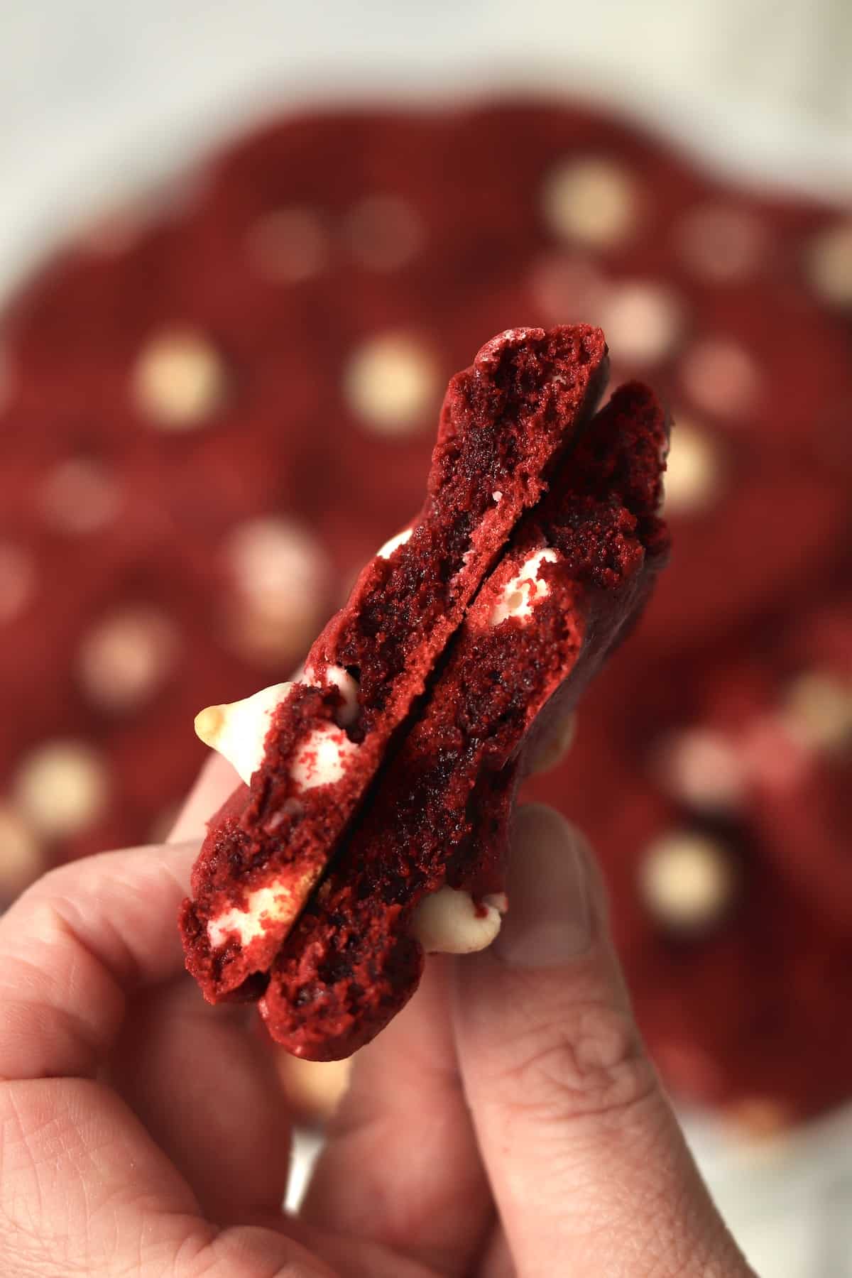 Hand holding a red velvet cookie that is broken in half to show chewy inside.