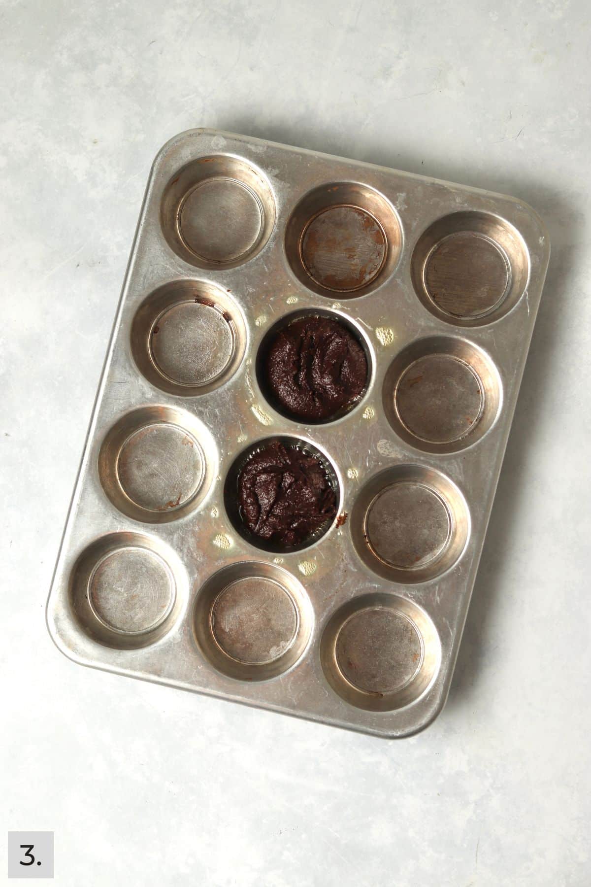 Brownie batter in two muffin cups.