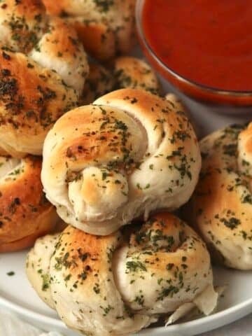 Plate of 4 ingredient garlic knots made with canned biscuits with a bowl of marinara sauce.