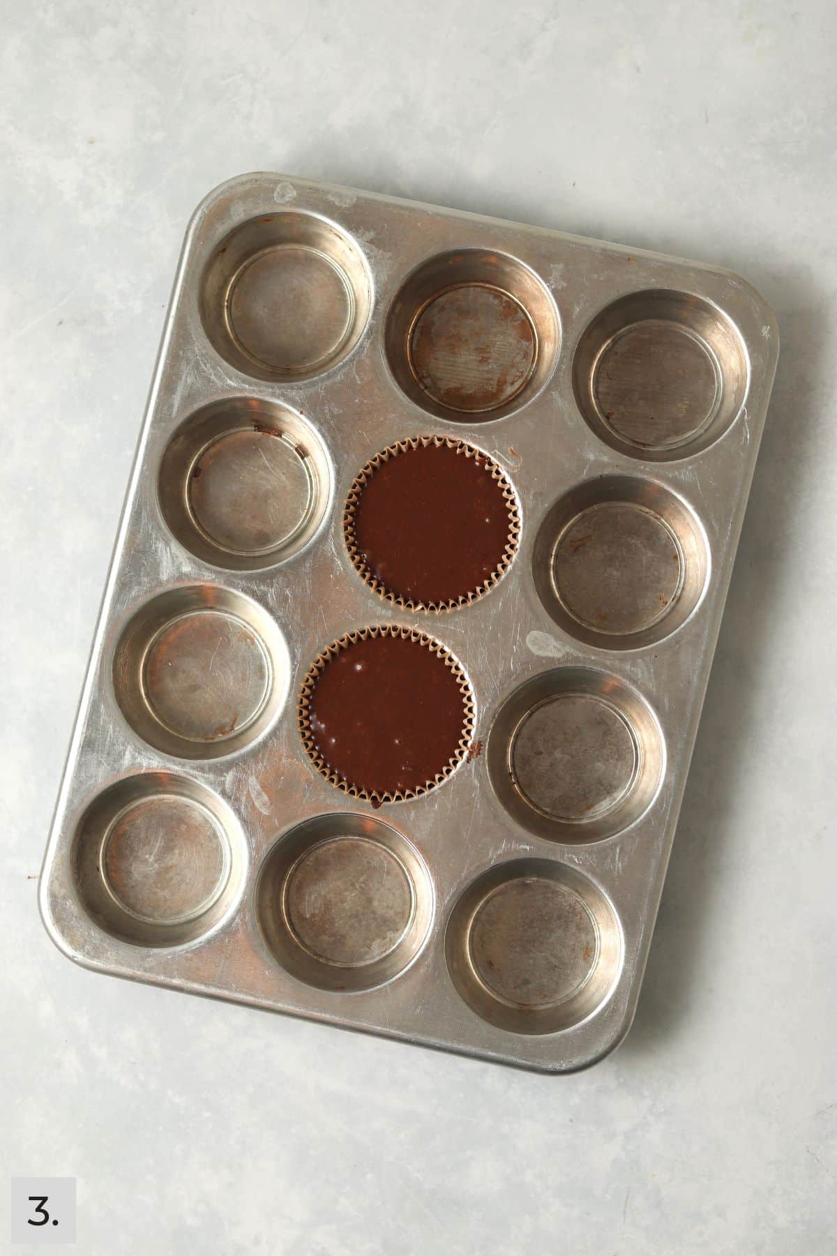 Two unbacked chocolate cupcakes in the muffin tin.