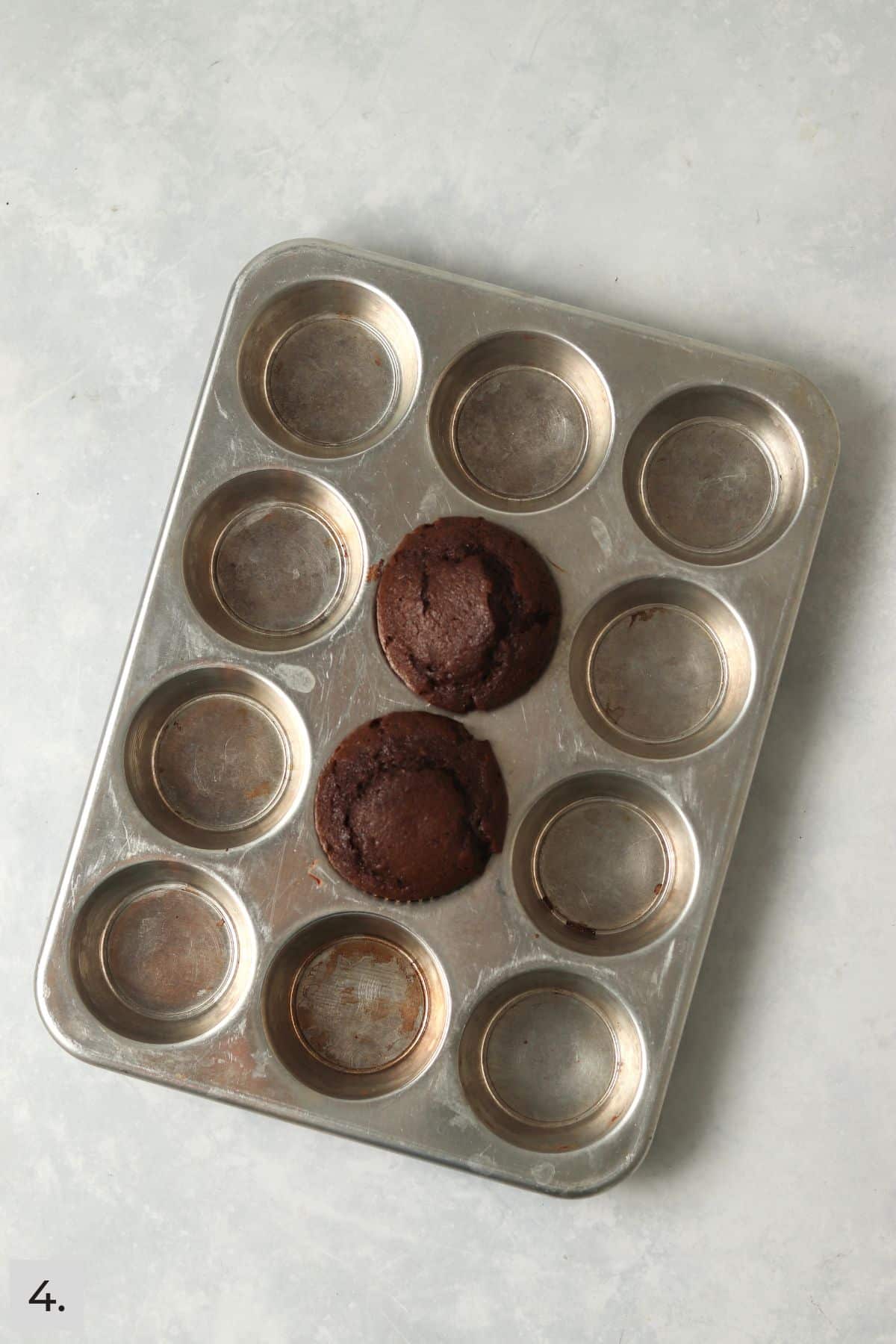 Two baked chocolate cupcakes in the muffin tin.