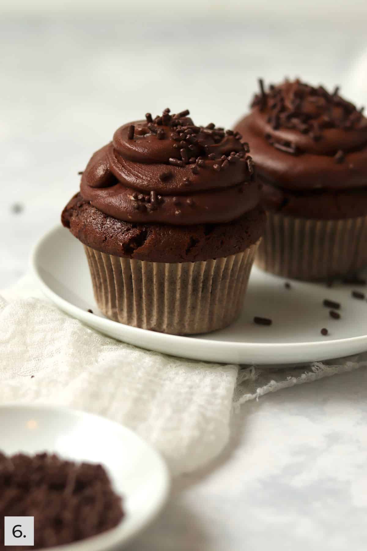 Two frosted chocolate cupcakes with chocolate sprinkles.