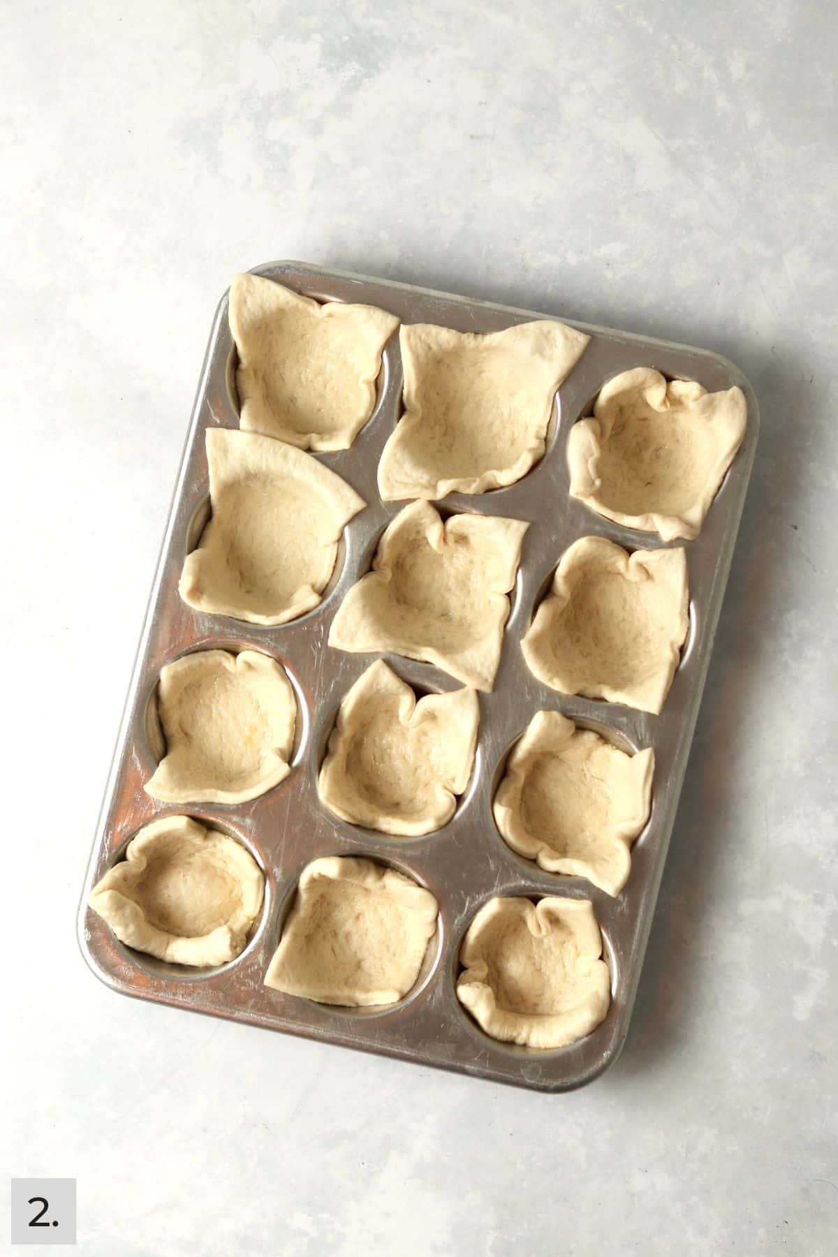 Pizza dough pressed into a muffin pan.