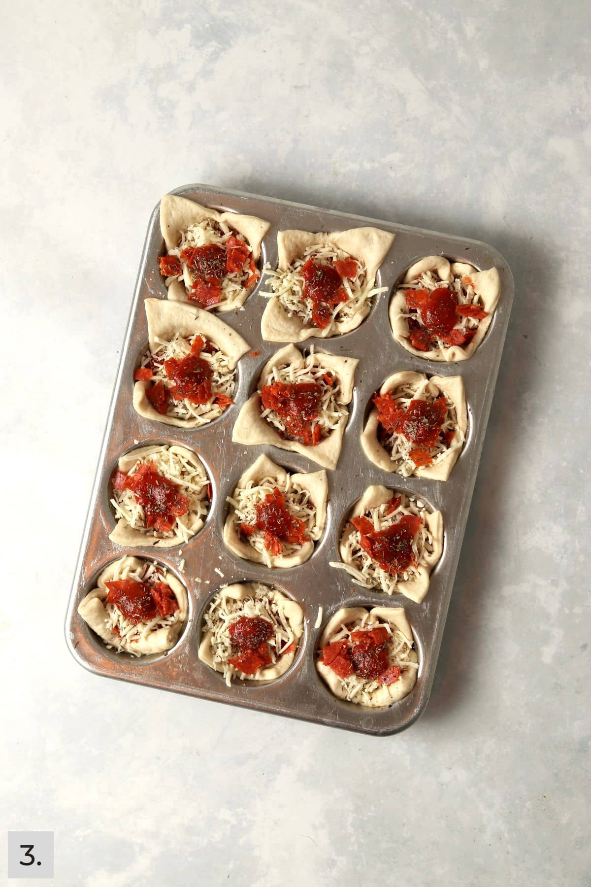 Unbaked pizza cups in a muffin pan with pepperoni and cheese.