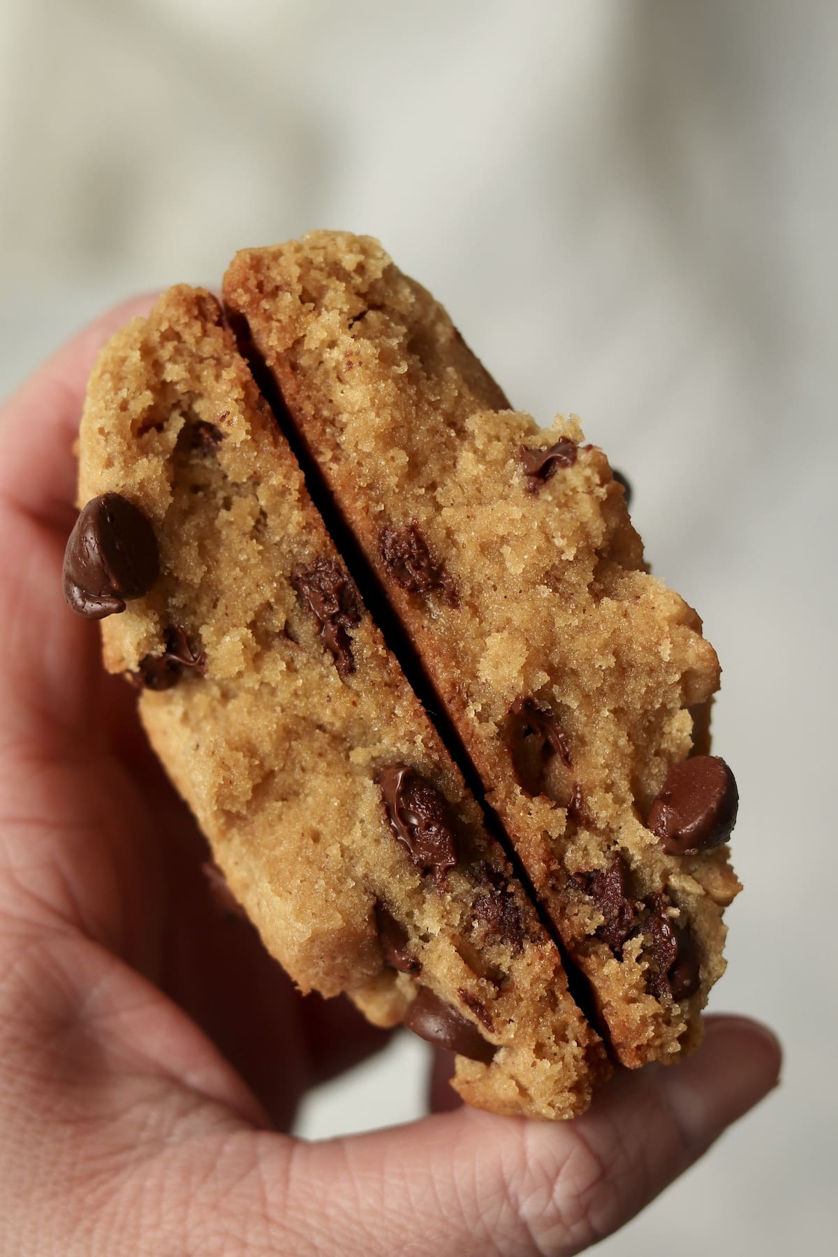 Hand holding a single serve brown butter chocolate chip cookie that is broken in half to show tender inside.