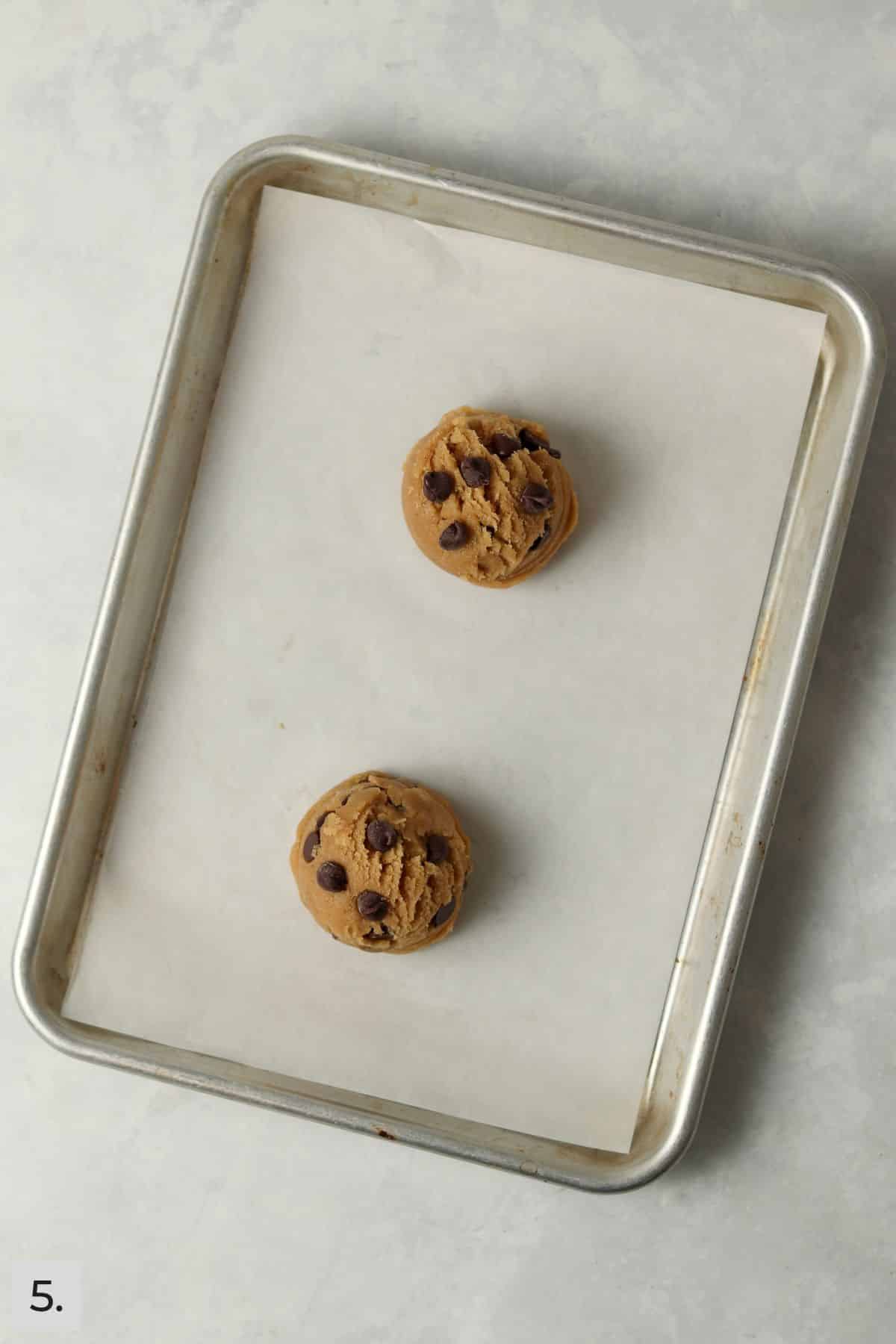 Two brown butter chocolate chip cookie dough balls on a baking sheet.