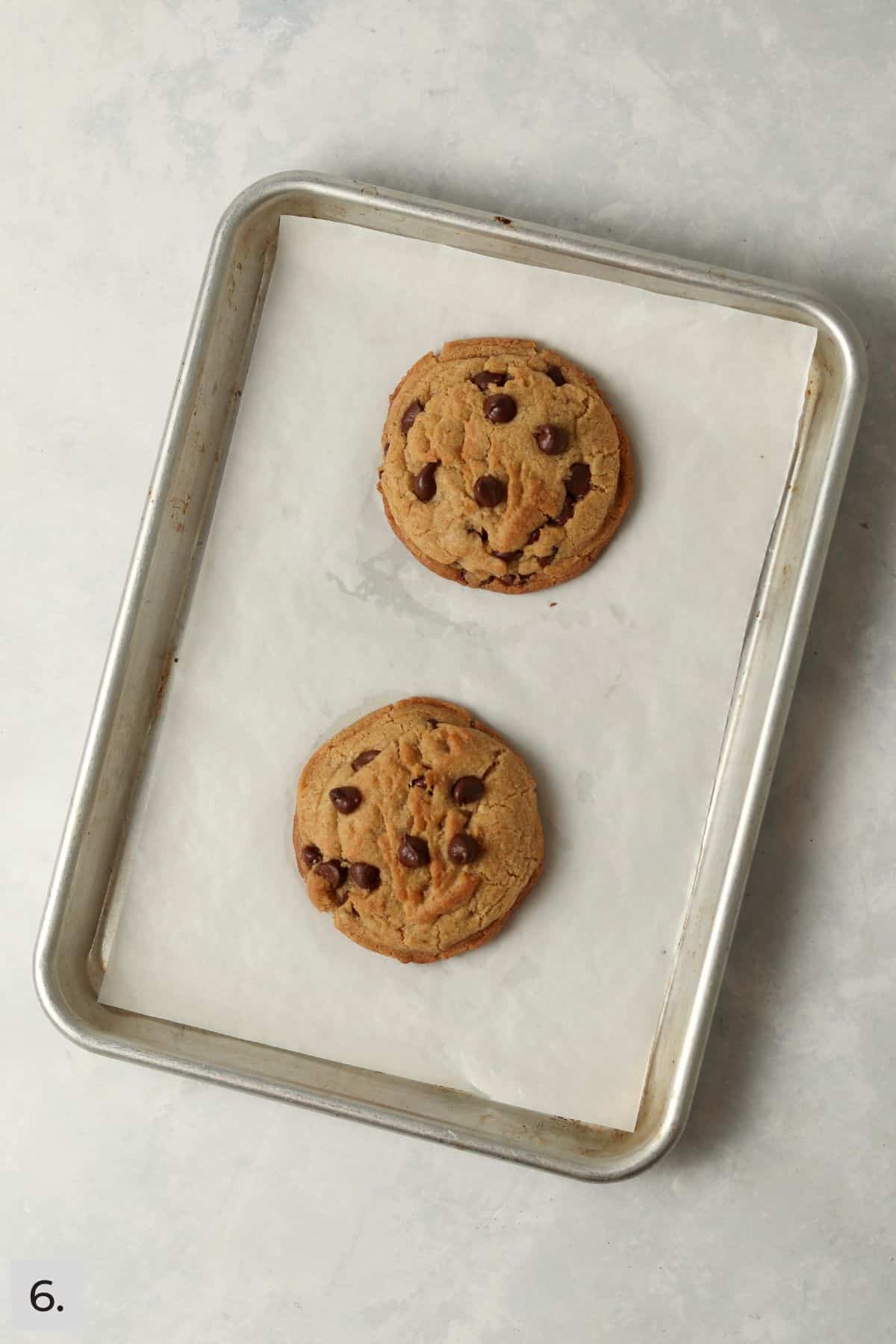 Two baked brown butter chocolate chip cookies on a baking sheet.