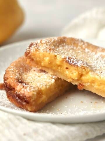 A single serve lemon bar cut in half on a plate with a whole lemon in the background.