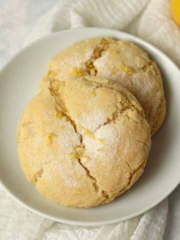 Two lemon cookies on a plate with a fresh lemon in background.