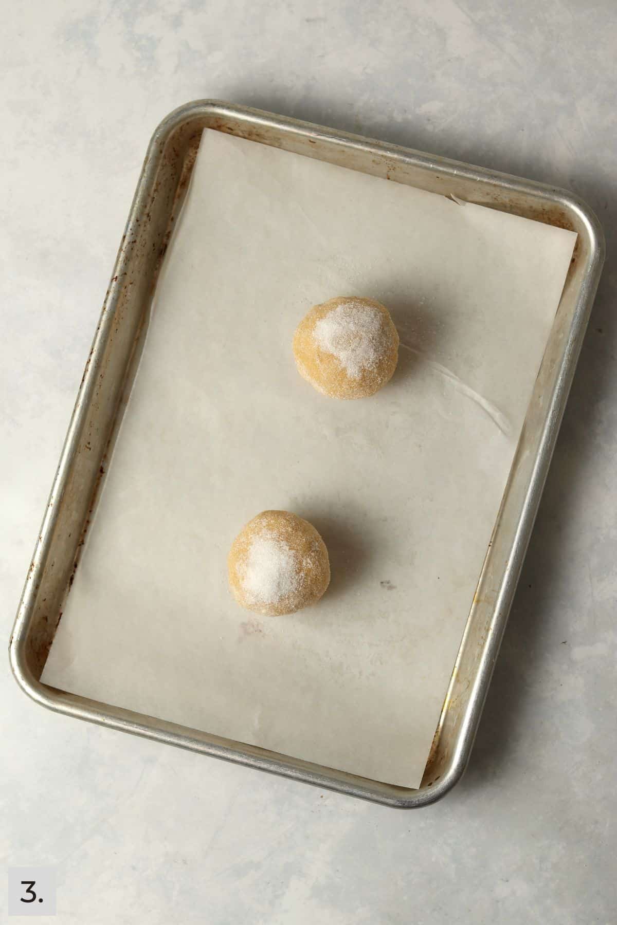 Two lemon cookie dough balls on a parchment lined baking sheet.
