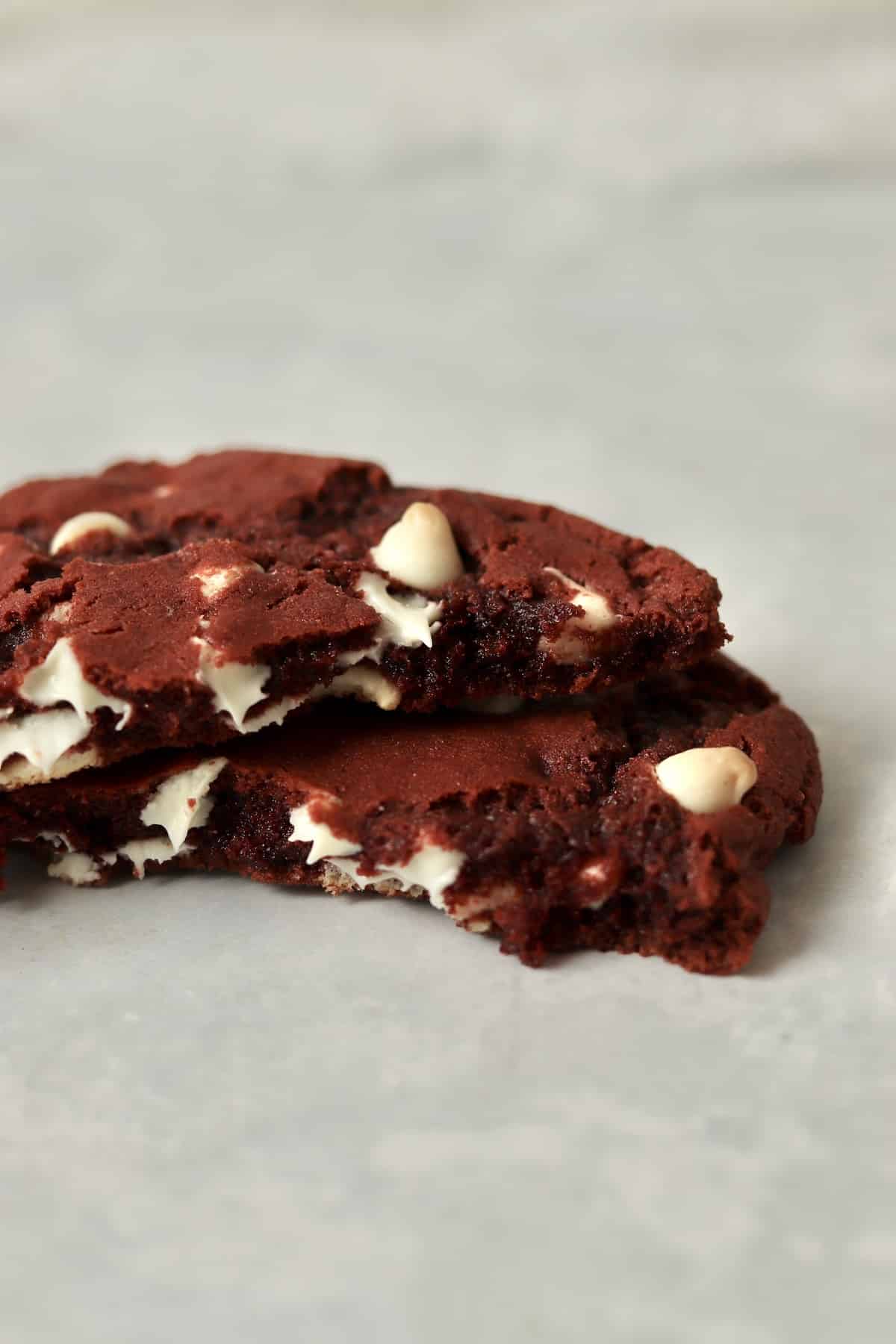 A single red velvet cookie broken in half to show tender inside and melted white chocolate chips.