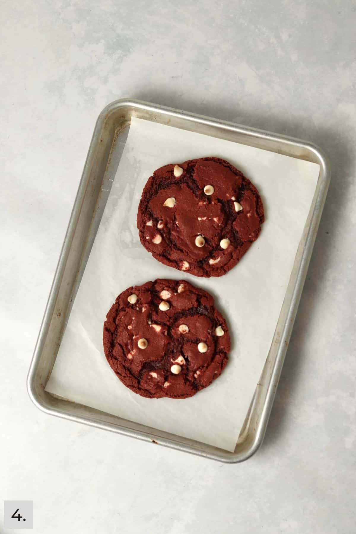 Two baked red velvet cookies on a small baking sheet.