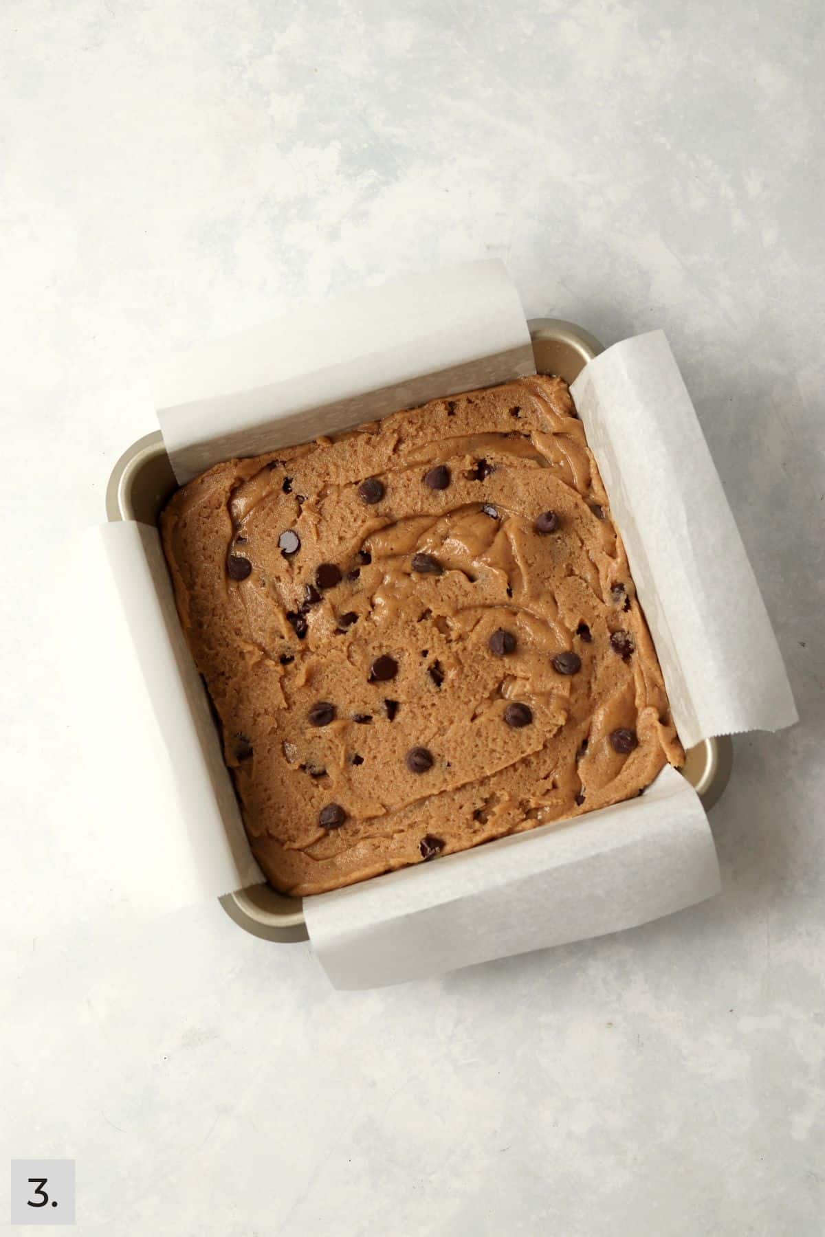 Unbaked almond butter chocolate chip bars in a square baking pan.