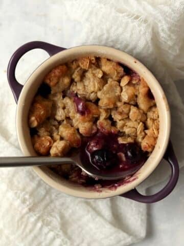 Single serve blueberry crisp in a ramekin with an oat topping.