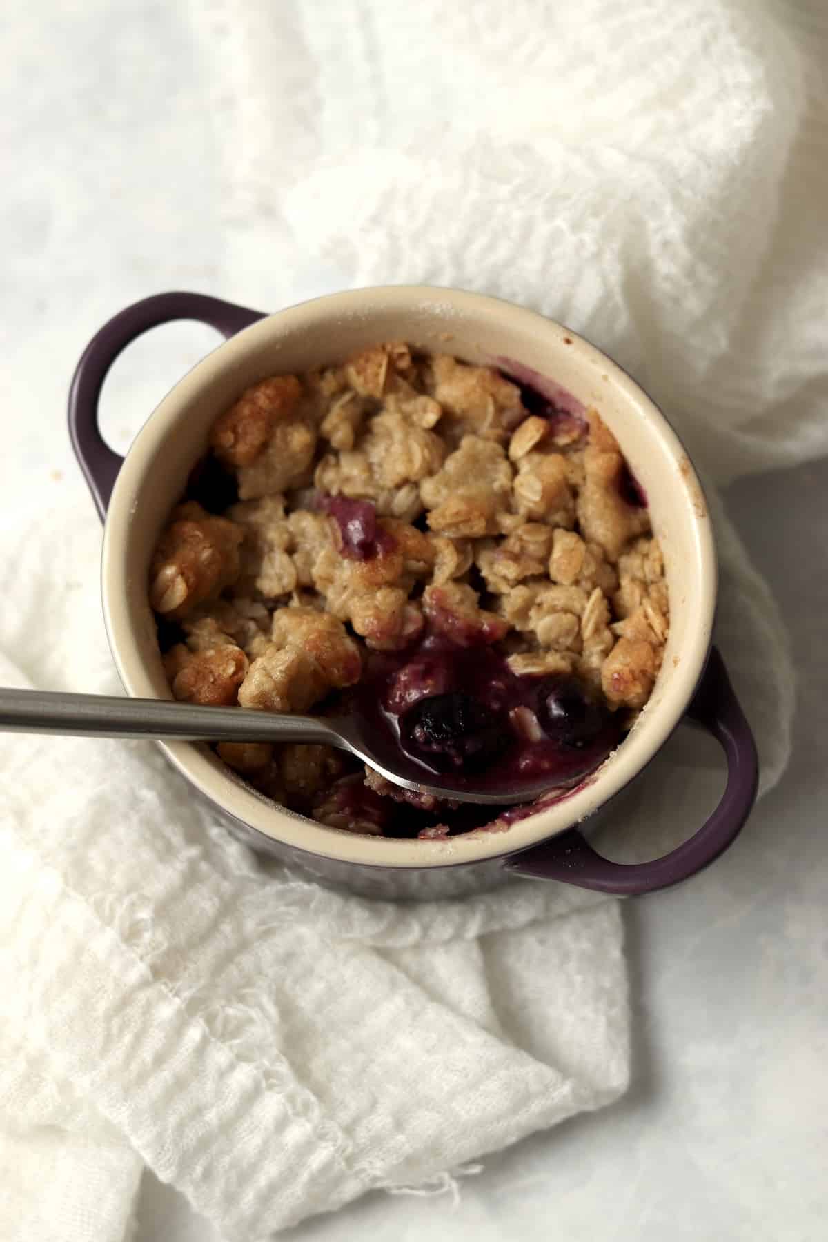 Single serve blueberry crisp in a ramekin with an oat topping.