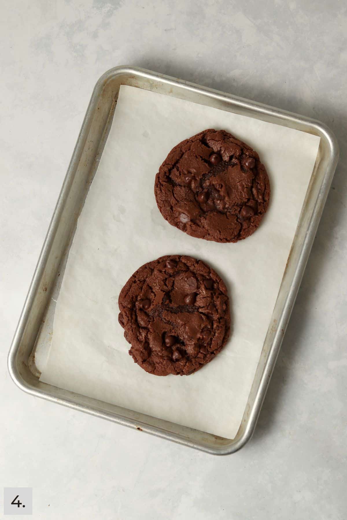 Two baked double chocolate cookies on a baking sheet.