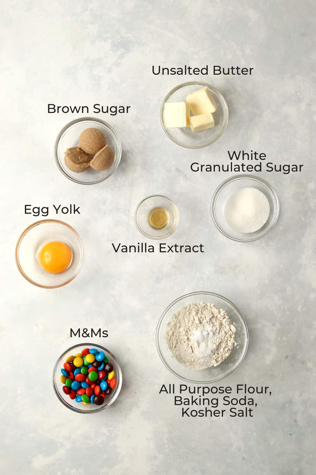 Ingredients to make a small batch of M&M cookies in small glass prep bowls.