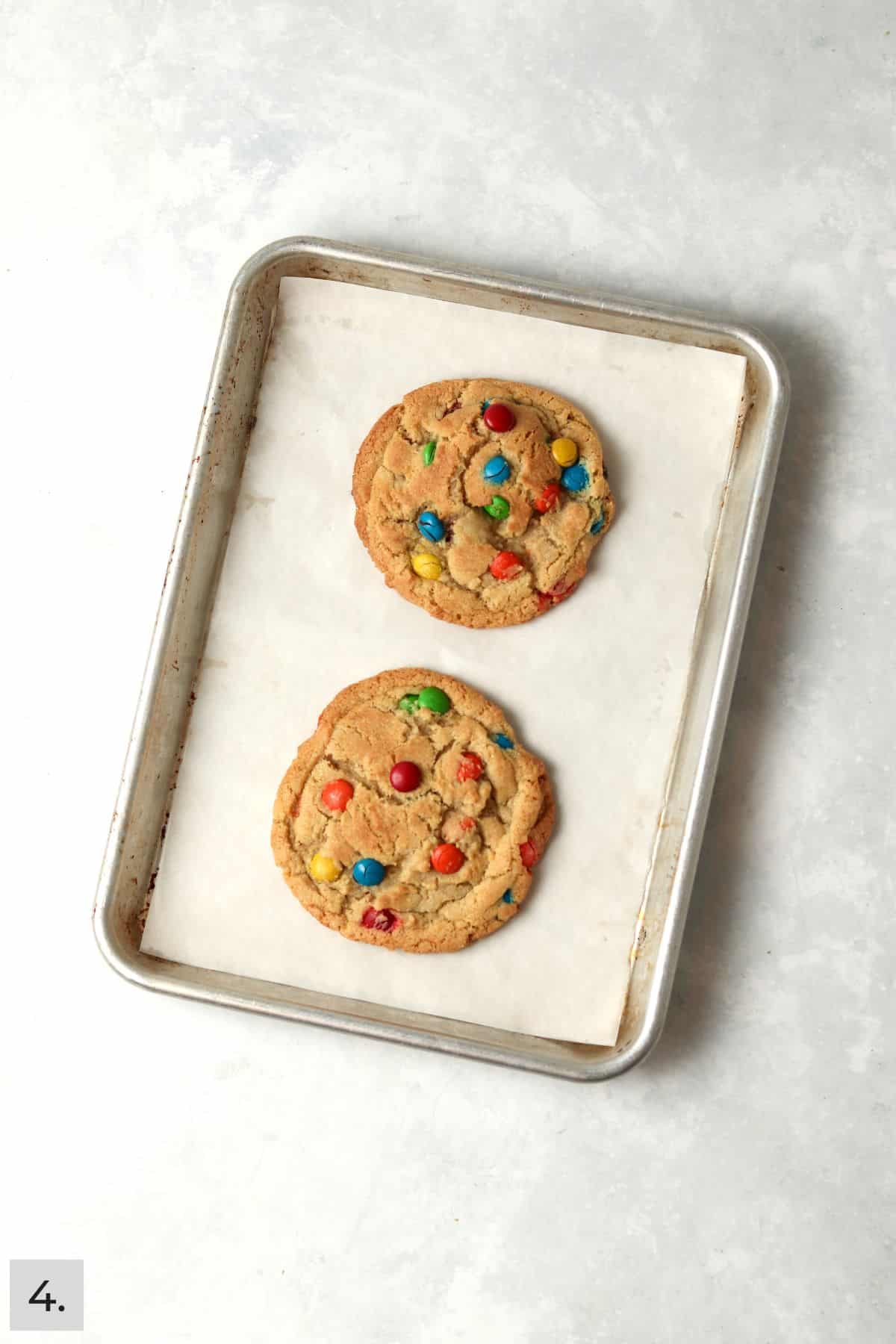 Two baked M&M cookies on a baking sheet.
