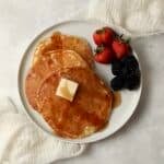 Single serve pancakes on a plate with maple syrup and berries.