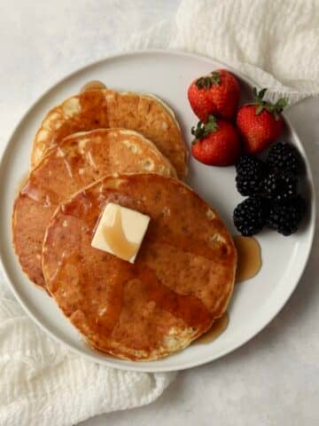 Single serve pancakes on a plate with maple syrup and berries.