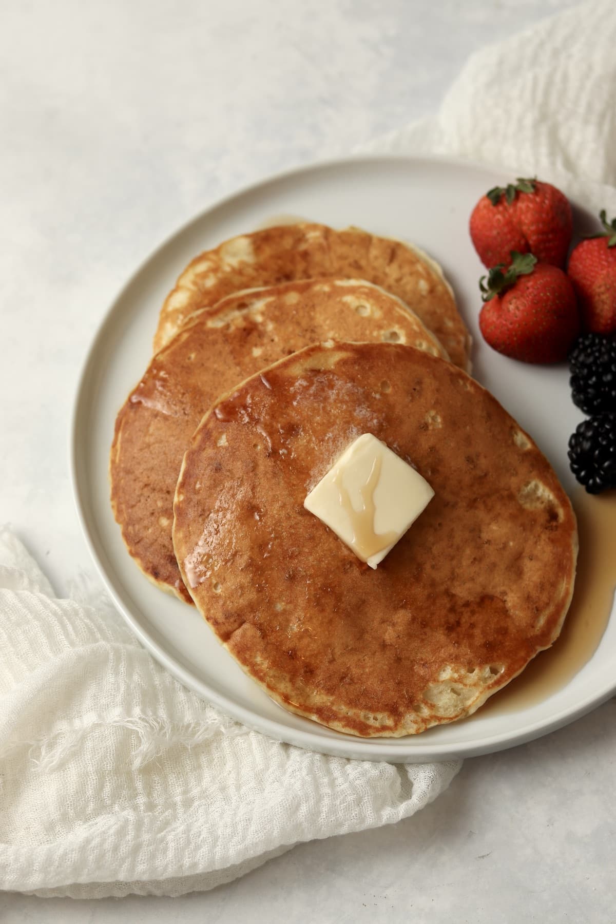 Single serve pancakes on a plate with maple syrup and berries.