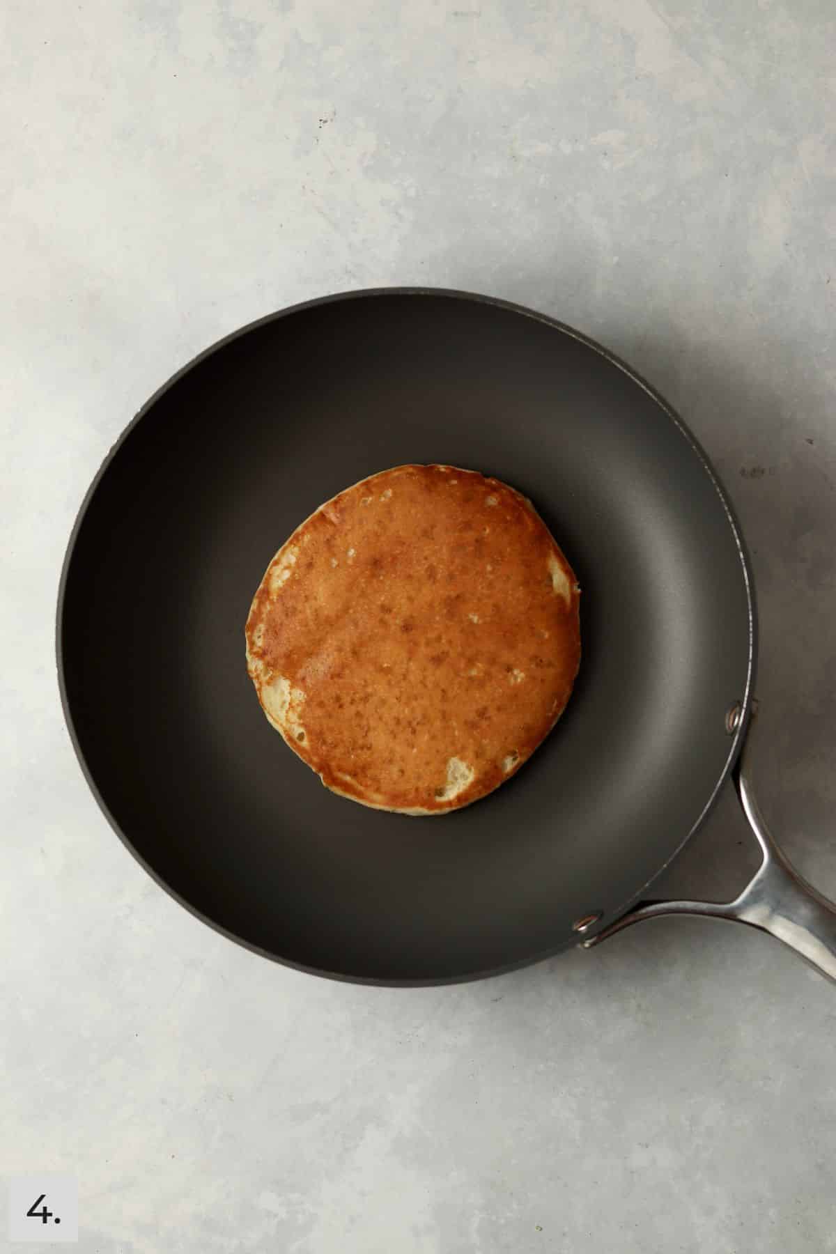 One pancake in nonstick skillet with golden brown coloring.