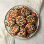 Pile of sprinkle sugar cookies on a plate with rainbow jimmies.
