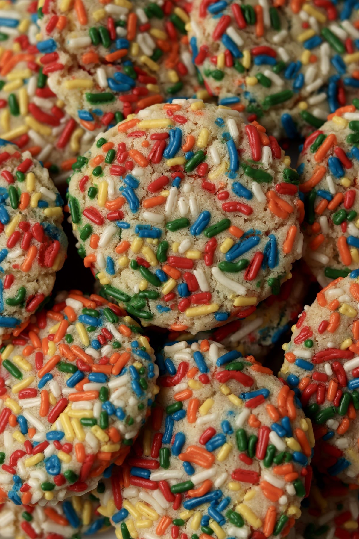 Pile of sprinkle sugar cookies with rainbow jimmies.