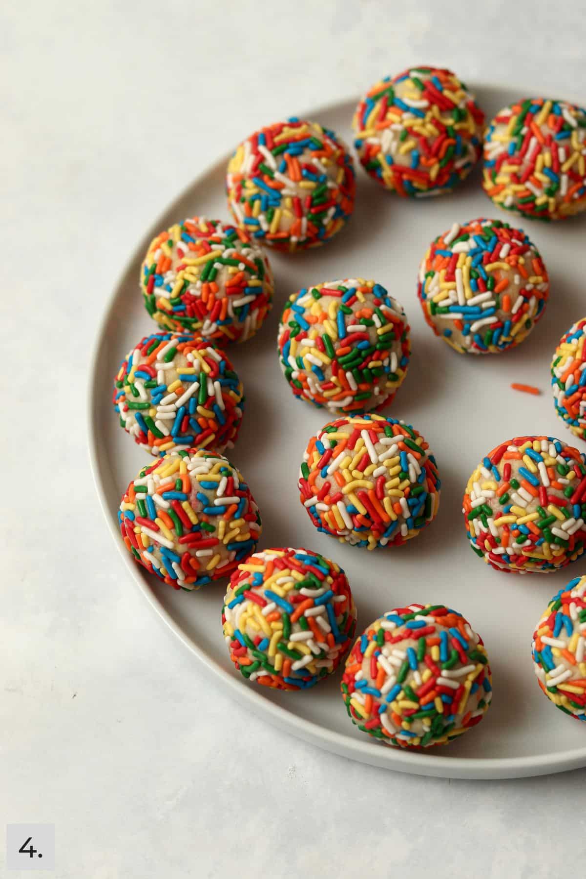 Sugar cookie dough balls rolled in sprinkles on a plate.