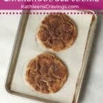 Two snickerdoodle cookies coated in cinnamon sugar on a baking sheet.