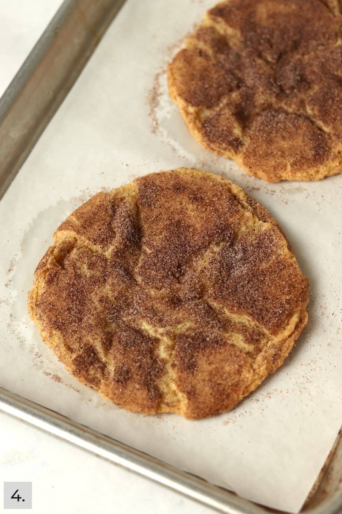 Two baked snickerdoodle cookies on a baking sheet.