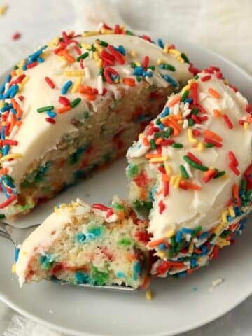 Single serve confetti cake cut in half with lots of rainbow sprinkles.