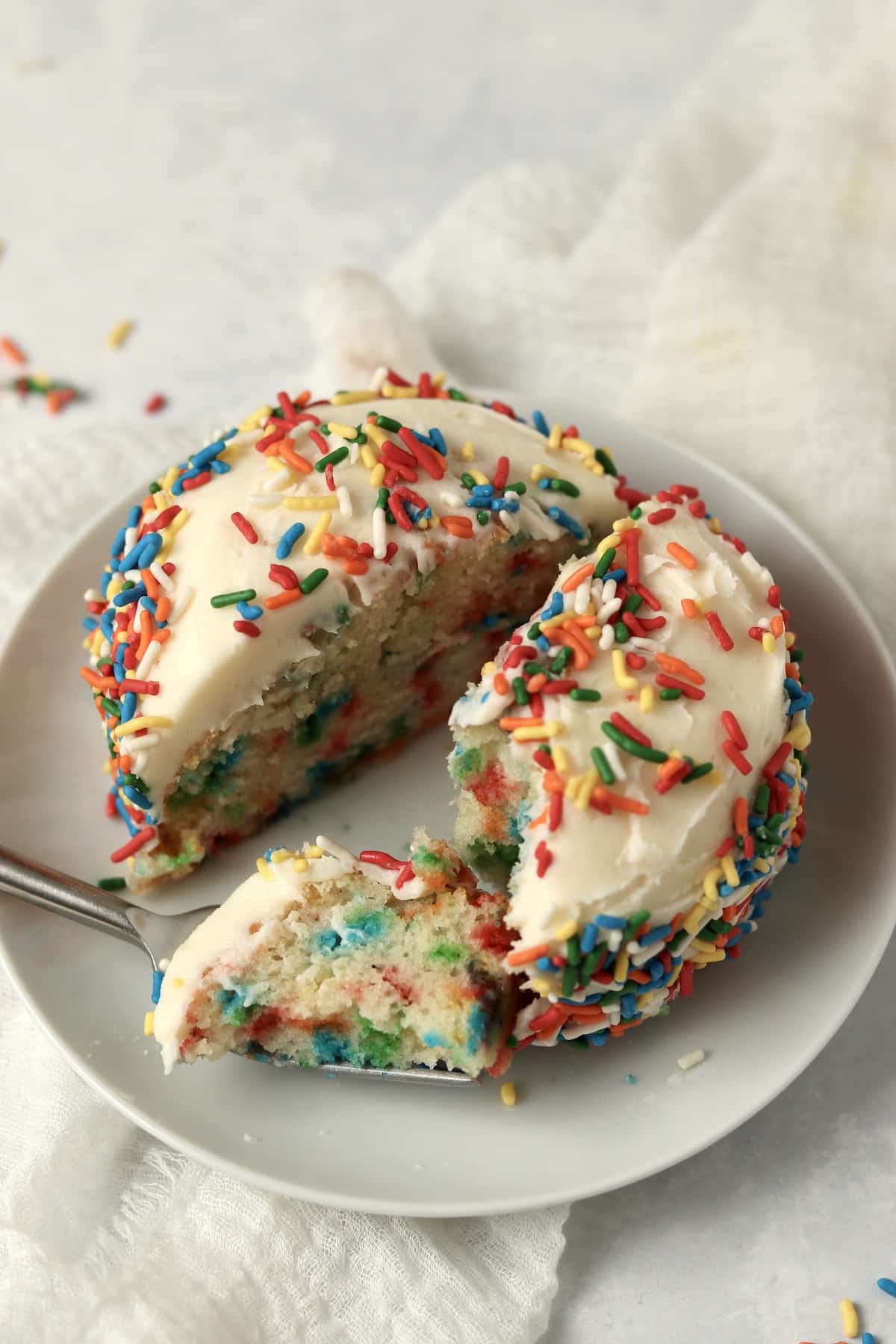 Single serve confetti cake cut in half with lots of rainbow sprinkles.