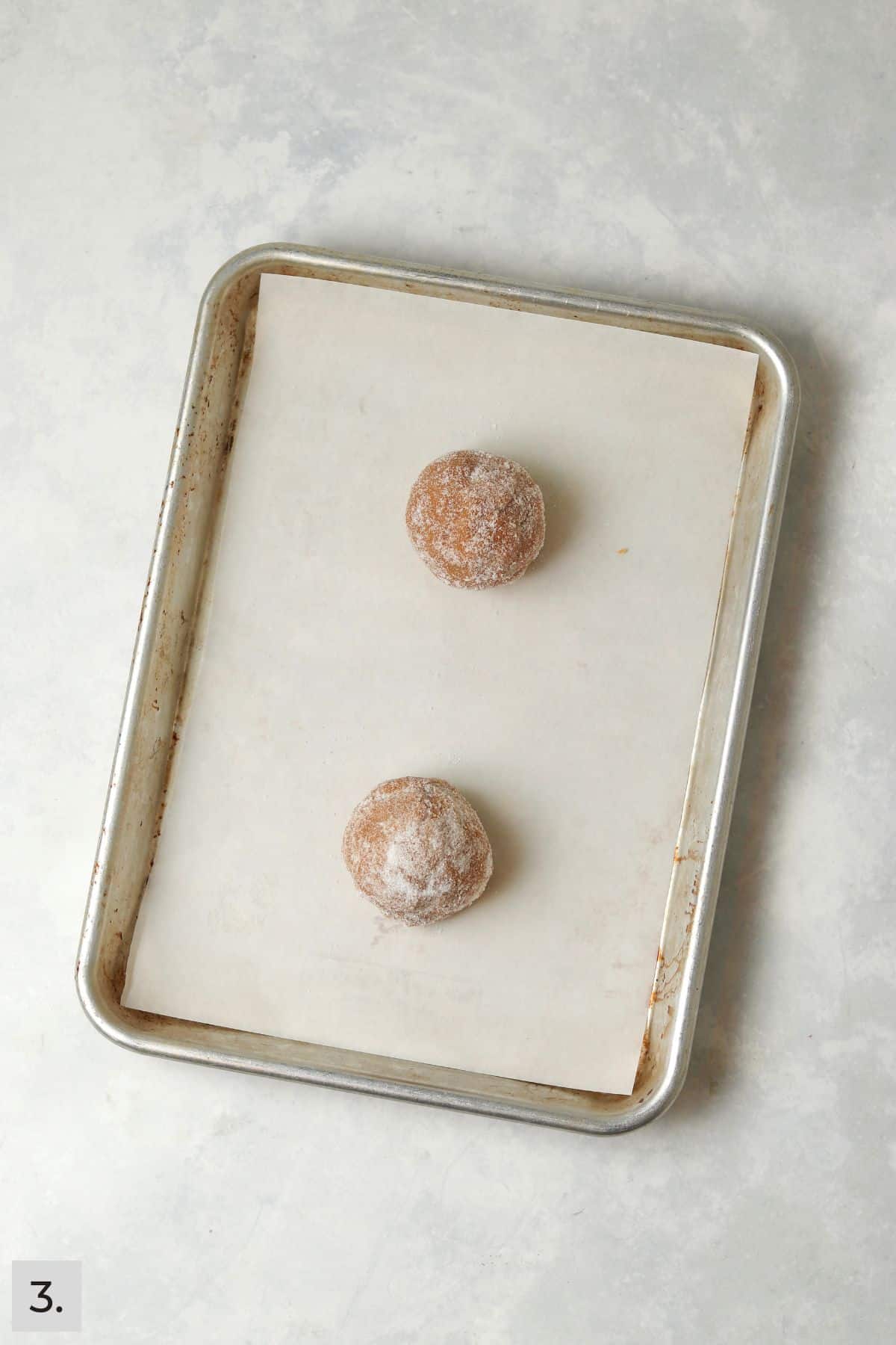 Two peanut butter cookie dough balls on a small cookie sheet.