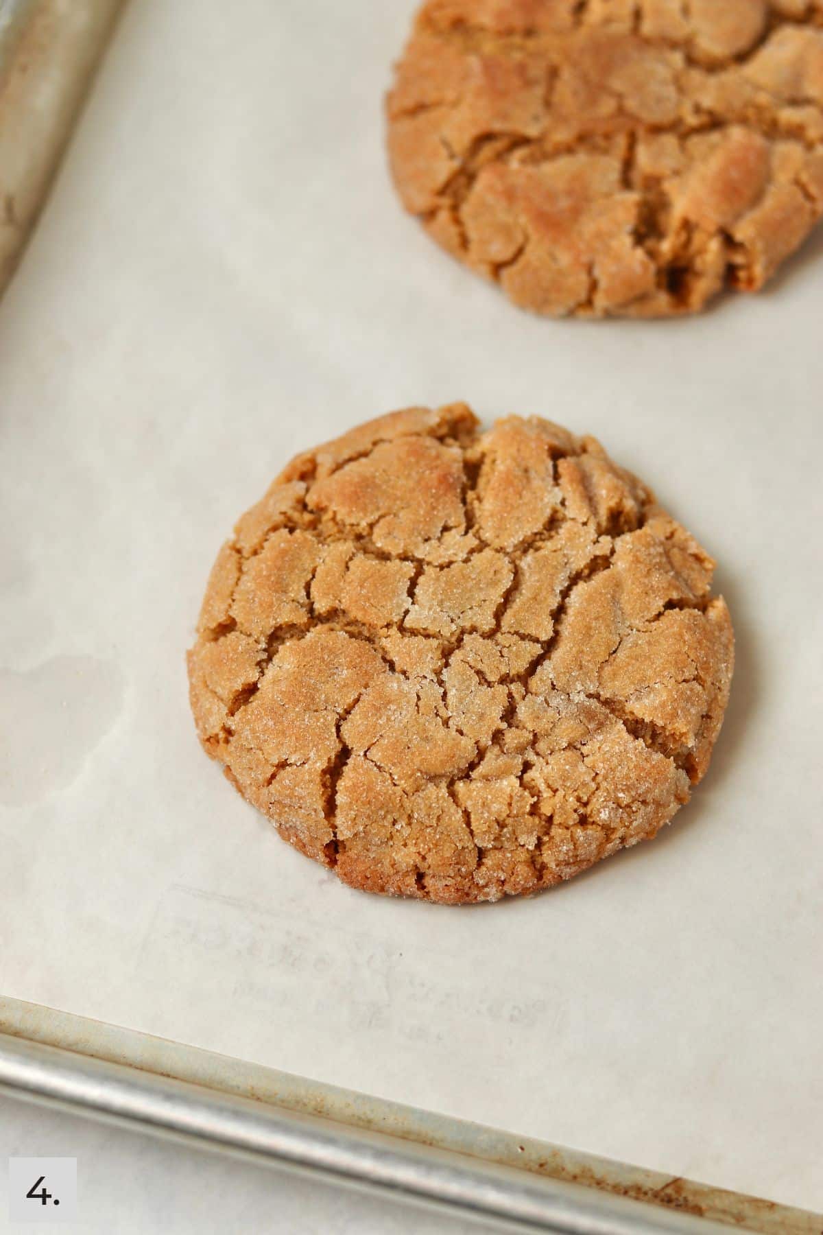 Two baked peanut butter cookies on a sheet pan.