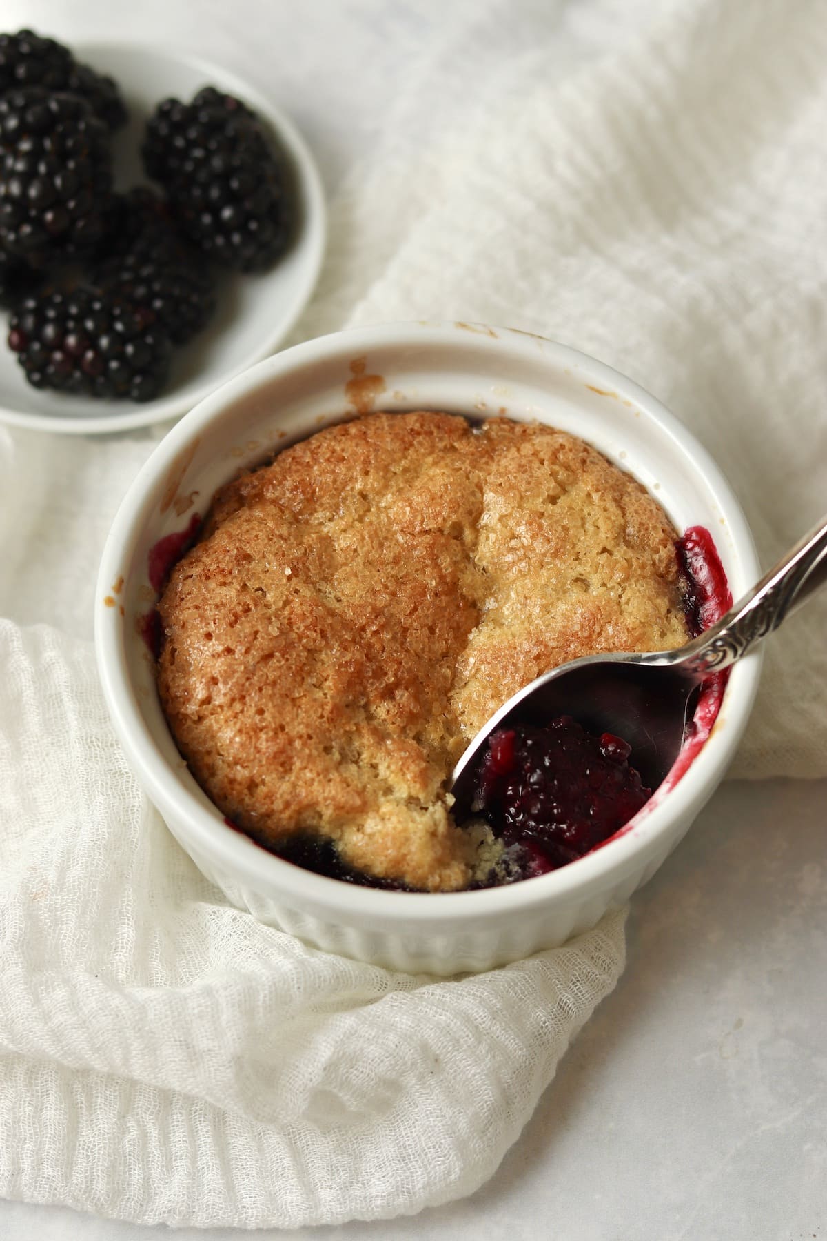 Single serve blackberry cobbler in a ramekin with fresh blackberries.