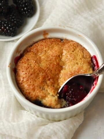 Single serve blackberry cobbler in a ramekin with fresh blackberries.
