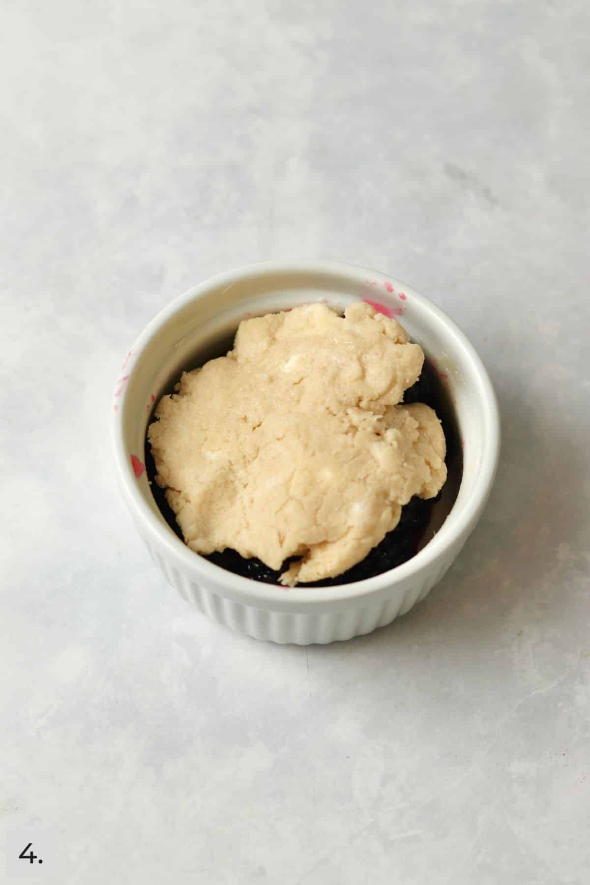 Blackberries in a ramekin topped with a cobbler topping before baking.