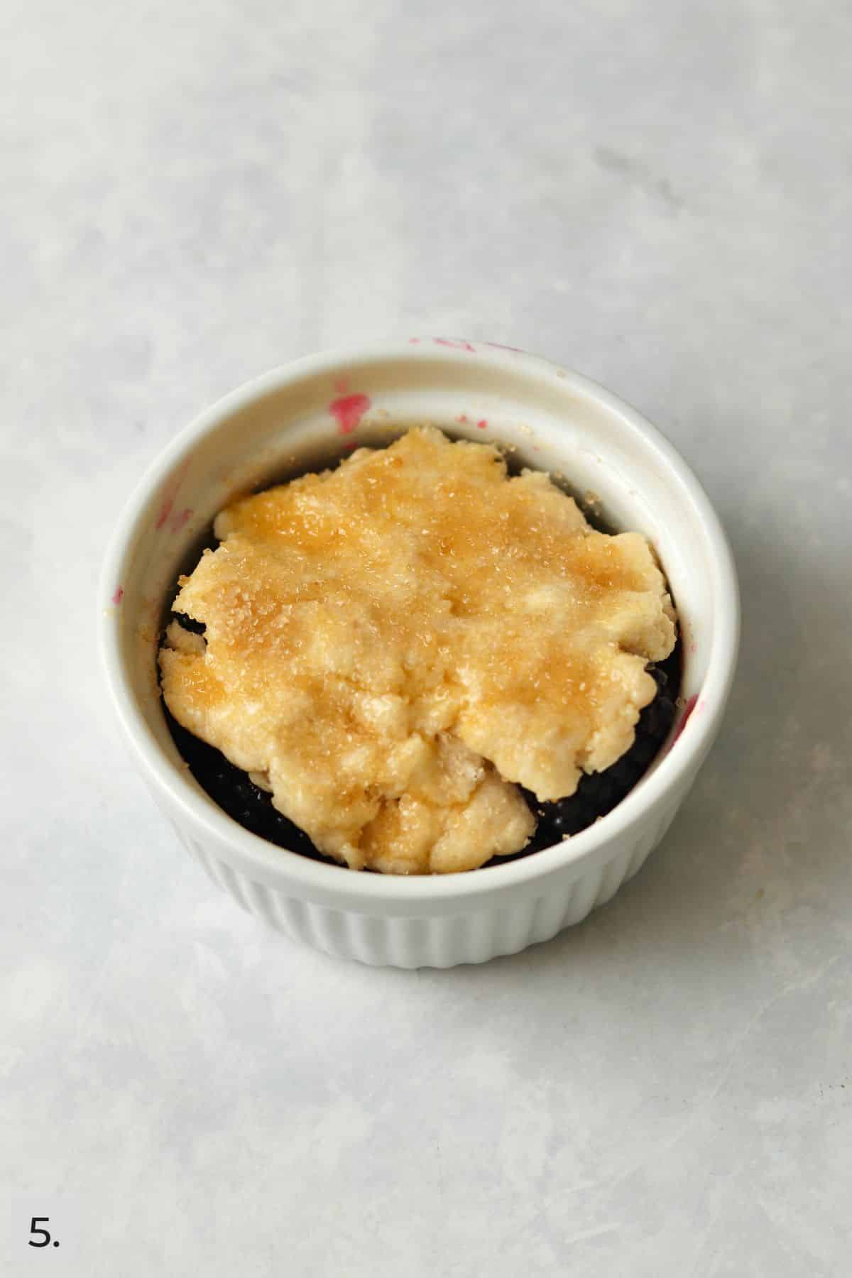 Unbaked blackberry cobbler in a ramekin brushed with an egg wash and sprinkled with sugar.