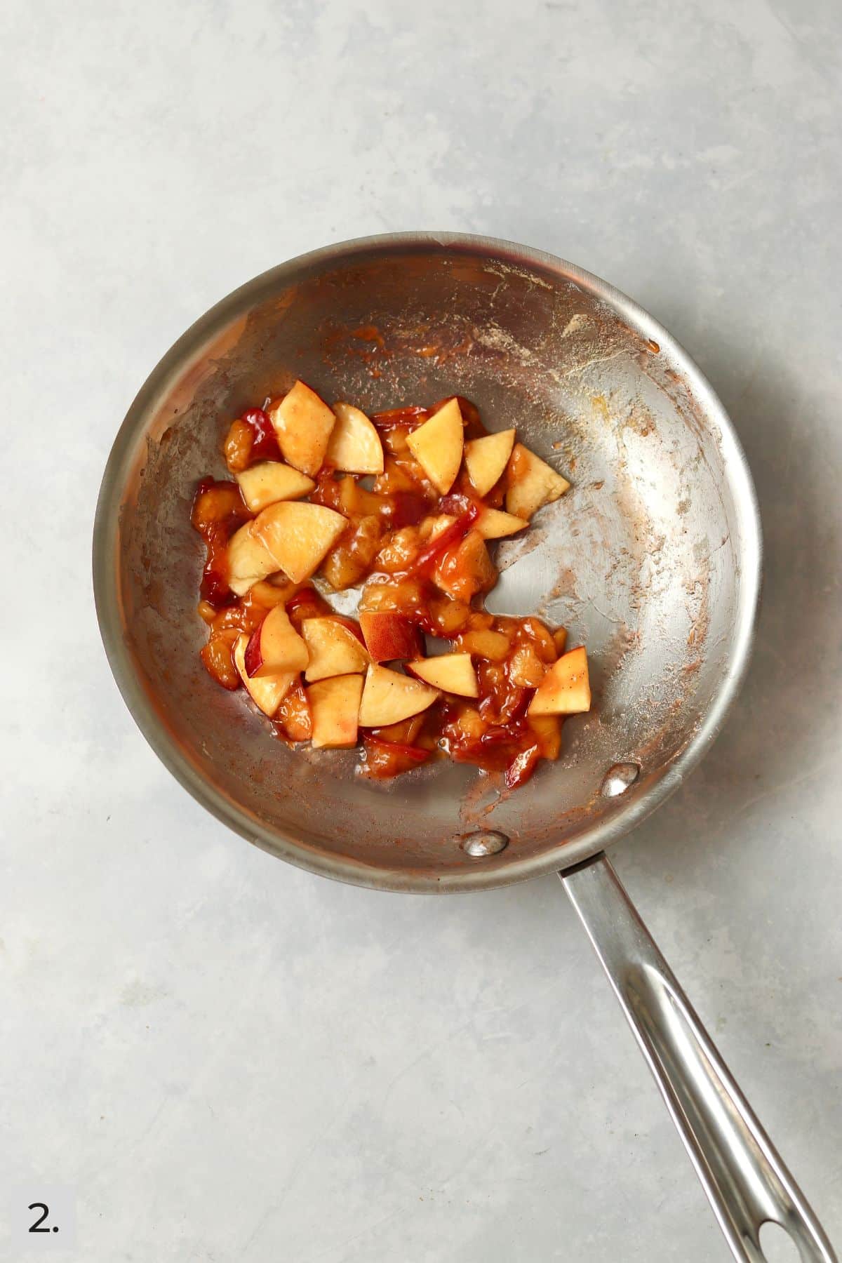 Cooked peaches and fresh peach slices in a small skillet.