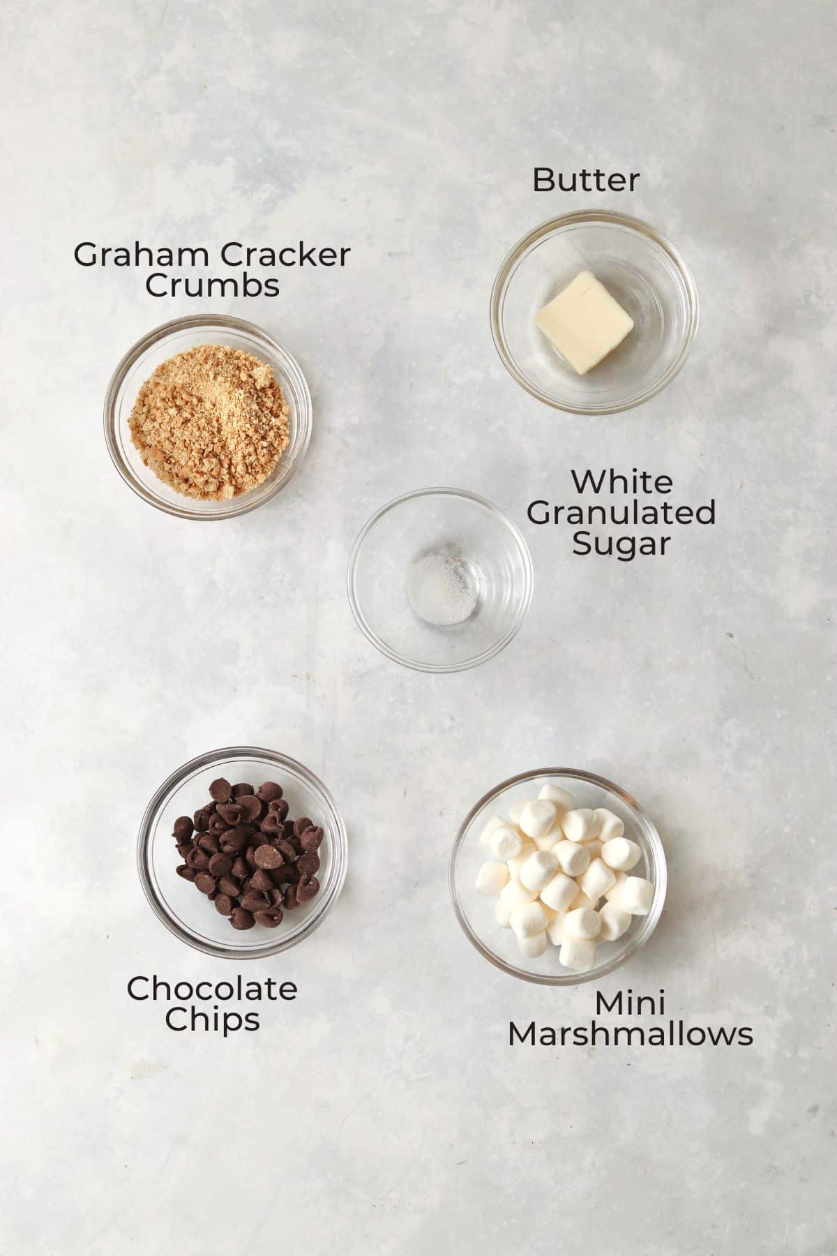 Graham cracker crumbs, mini marshmallows, chocolate chips, butter, and sugar in small glass prep bowls.