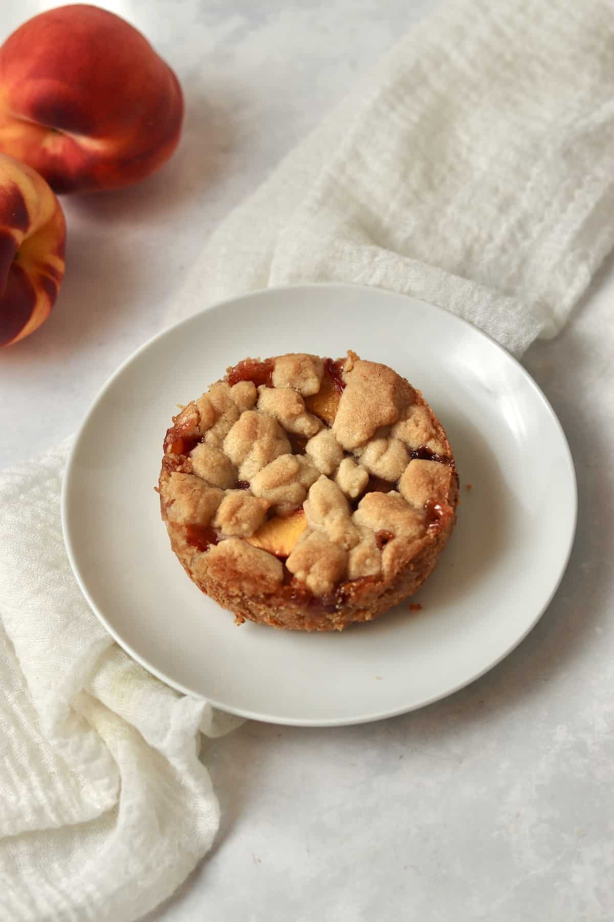 Single serve peach crumb bar on a plate with fresh peaches.