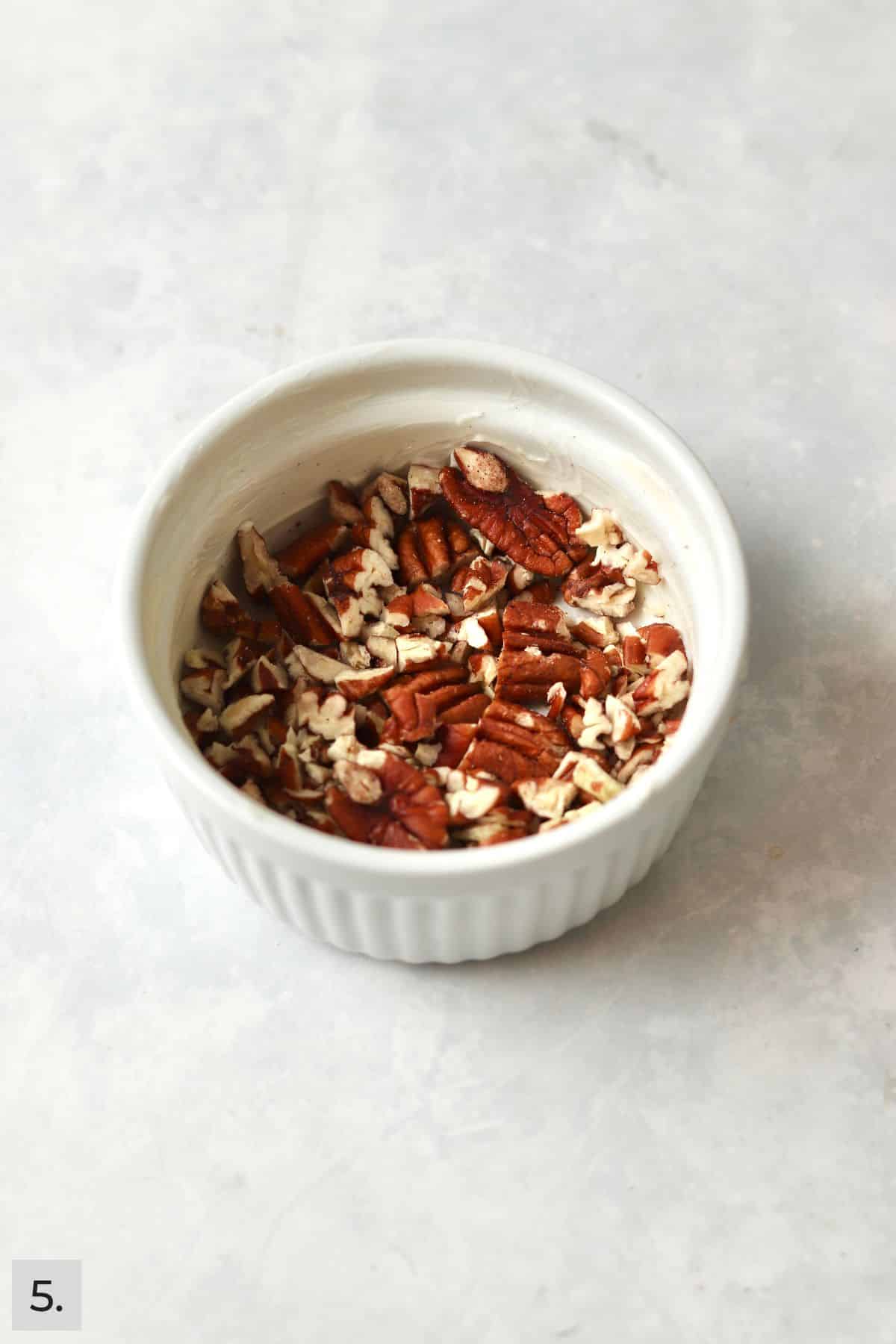 Chopped pecan halves in a greased ramekin.