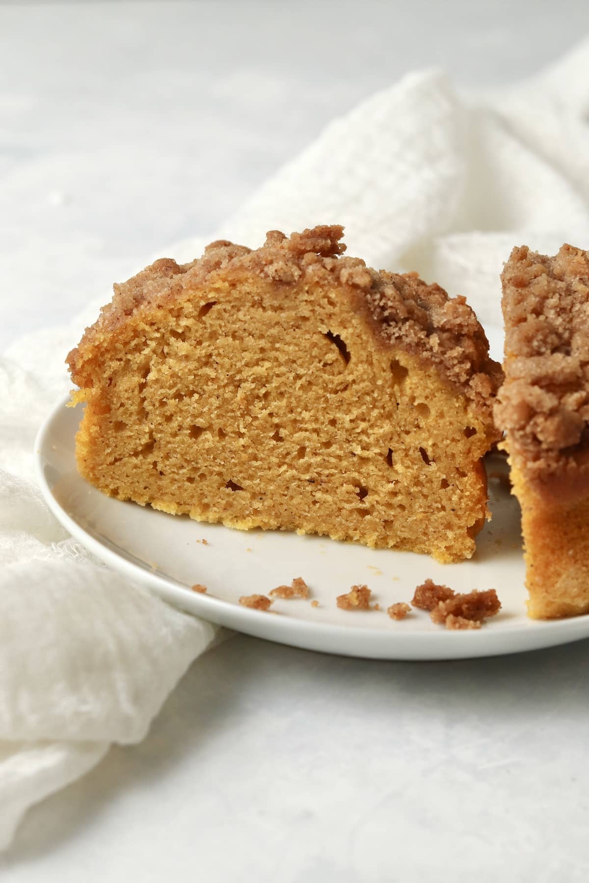 Single serve pumpkin coffee cake with streusel topping cut in half on a plate.