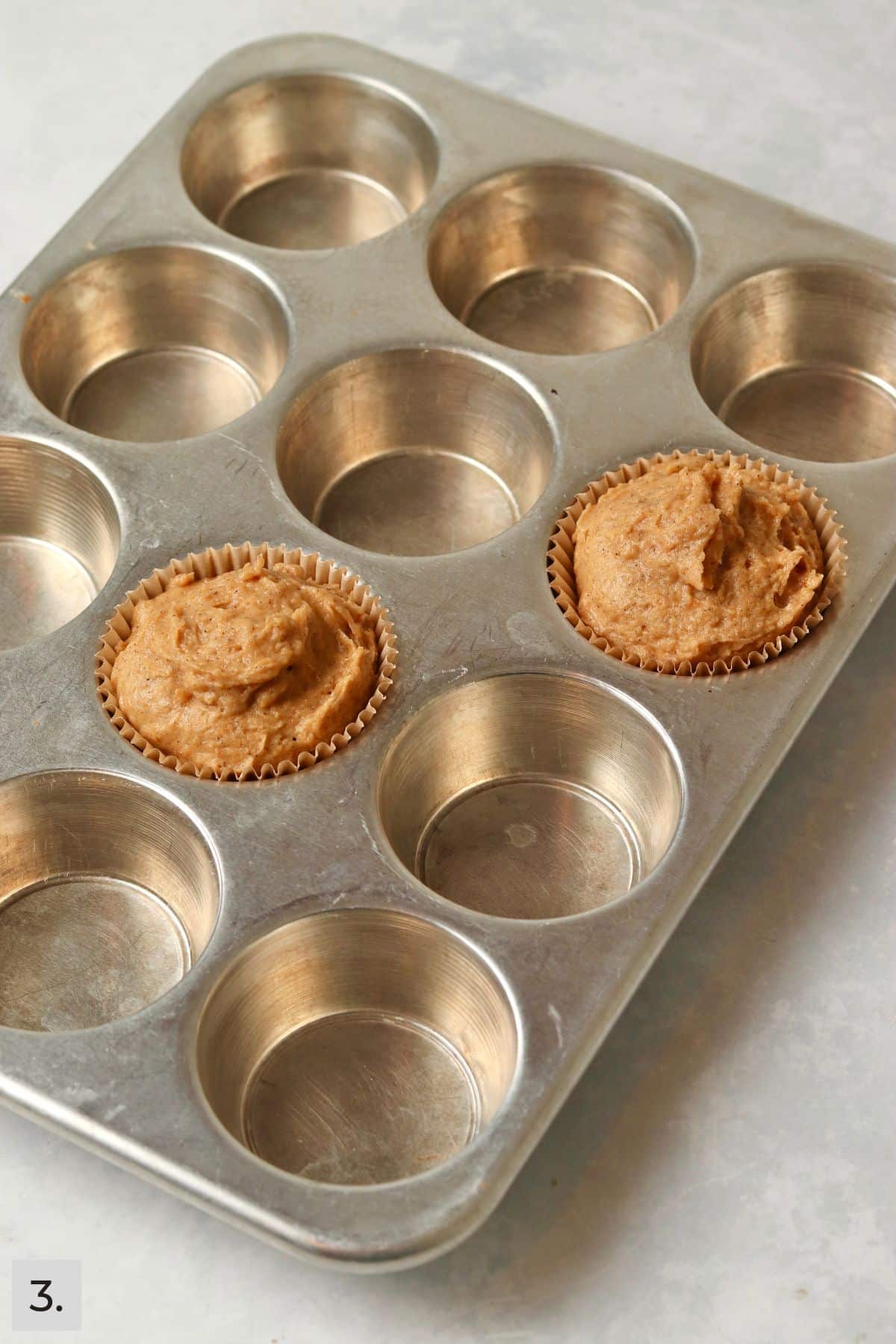 Pumpkin muffin batter in two muffin cups before baking.