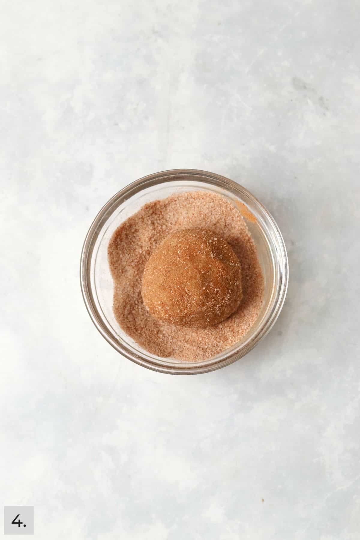 Pumpkin snickerdoodle cookie dough ball being rolled in cinnamon sugar.
