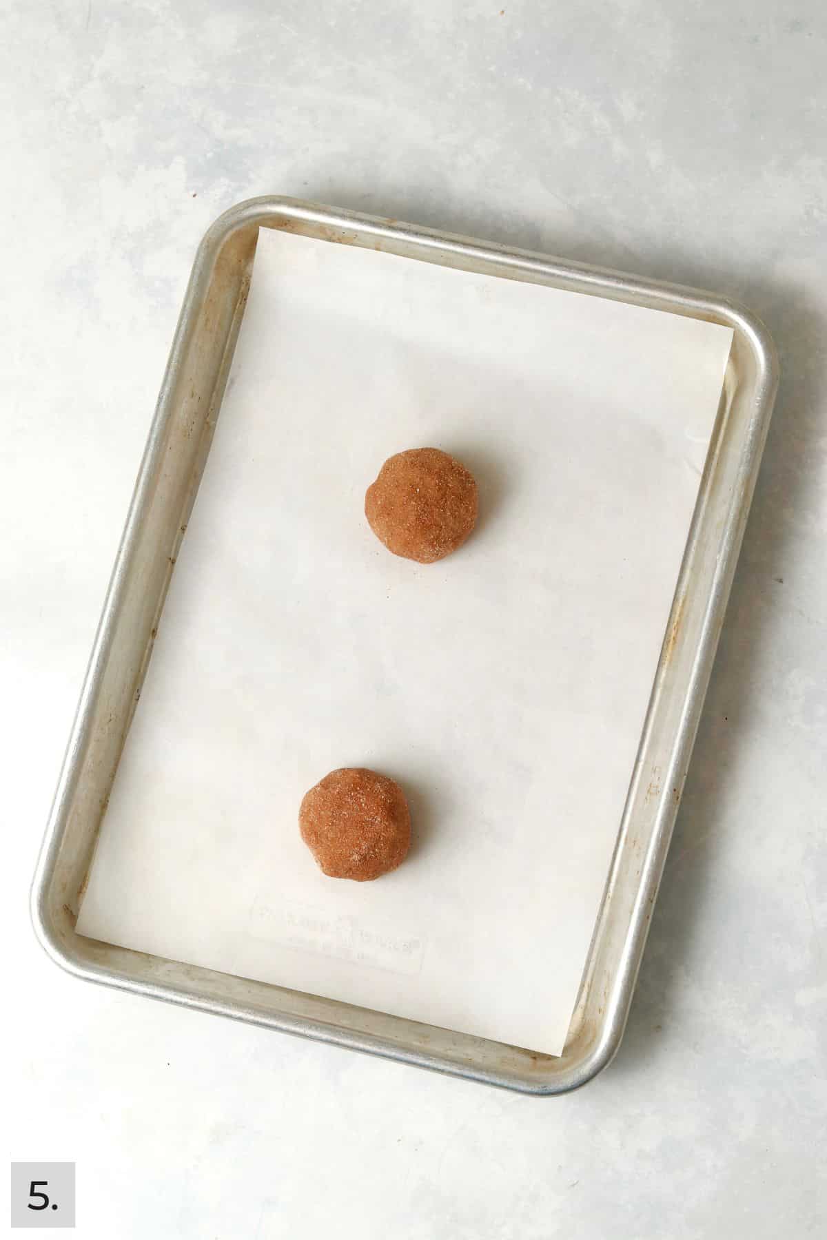 Two pumpkin snickerdoodle dough balls on a baking sheet.