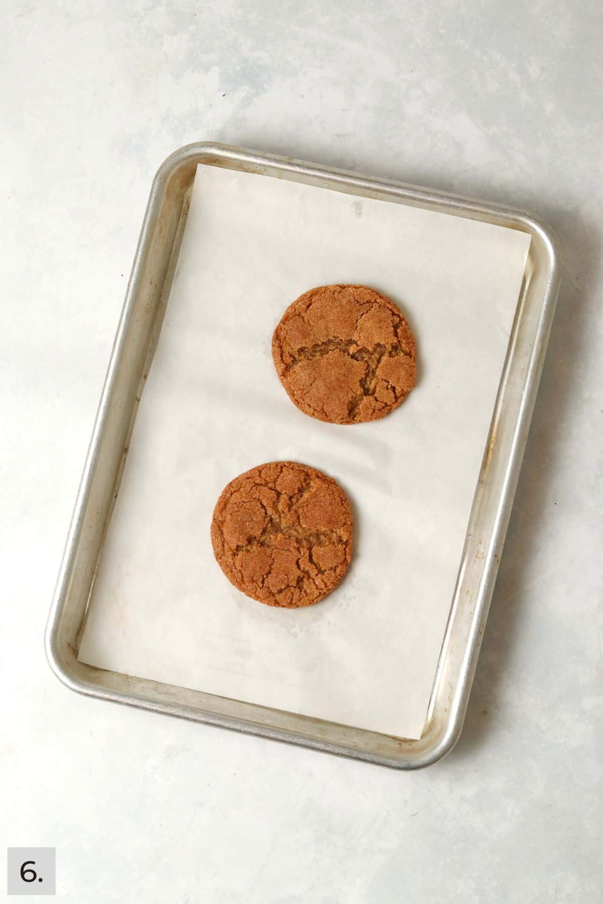 Two baked pumpkin snickerdoodle cookies on a baking sheet.